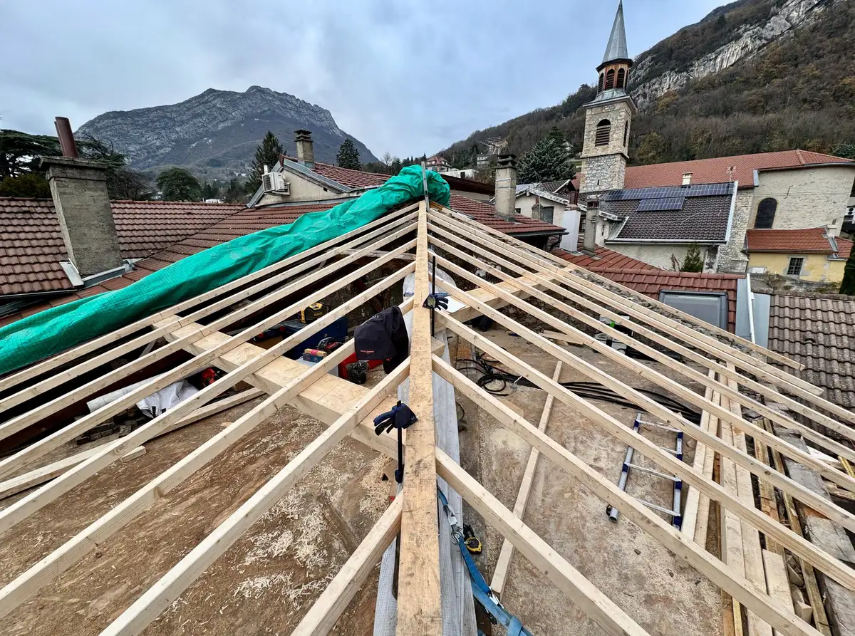Charpente neuve montée sur un bâti de village, arêtier et chevrons posés avant couverture.