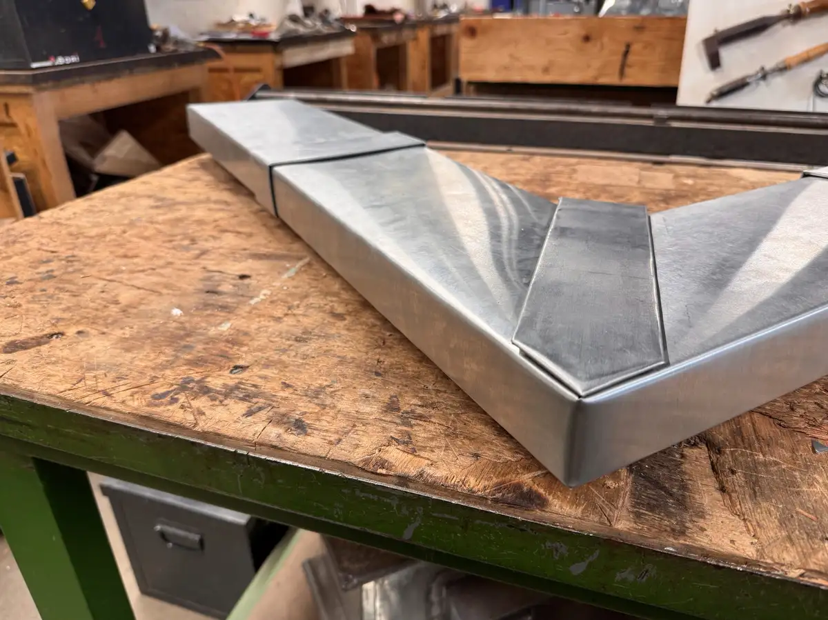 Pièce de zinc pliée en angle posée sur un établi d'atelier, plis nets et surface satinée.