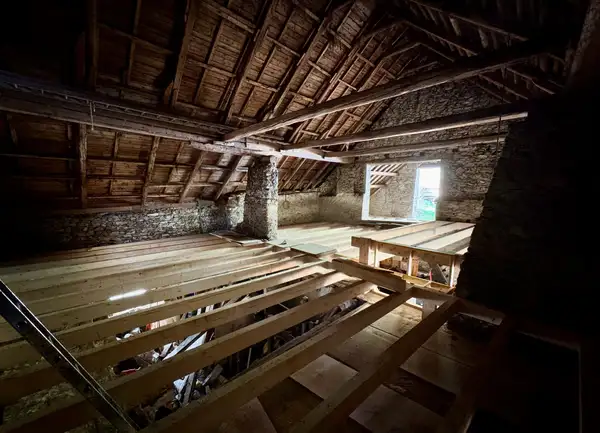 Comble ancien aux murs de pierre, solives neuves en bois clair posées sous une charpente d'origine.